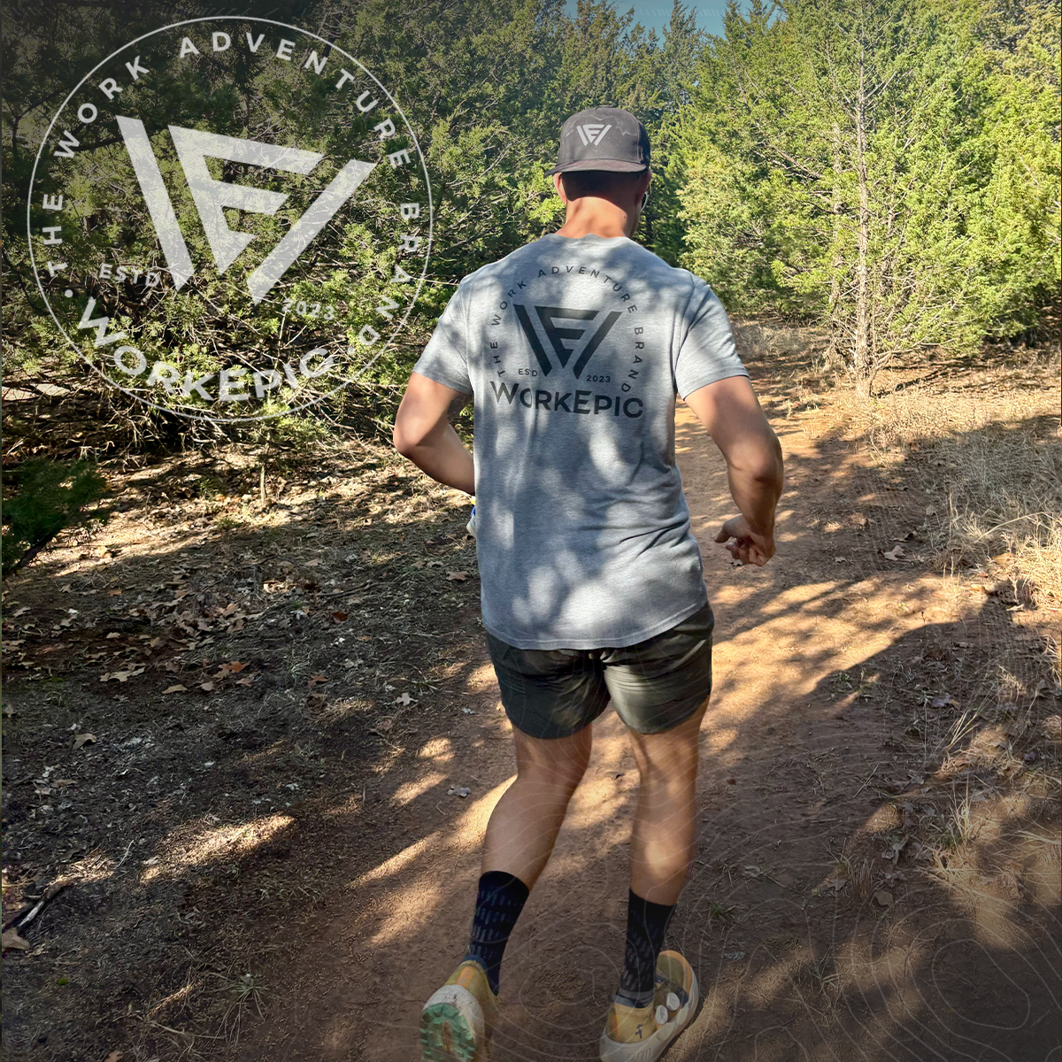 A man running on a trail in the woods wearing a grey Work Epic shirt