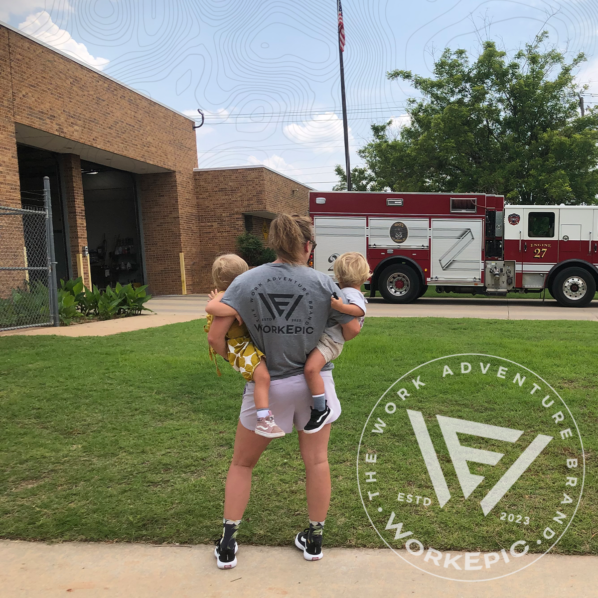 A woman wearing a grey Work Epic shirt by a fire truck