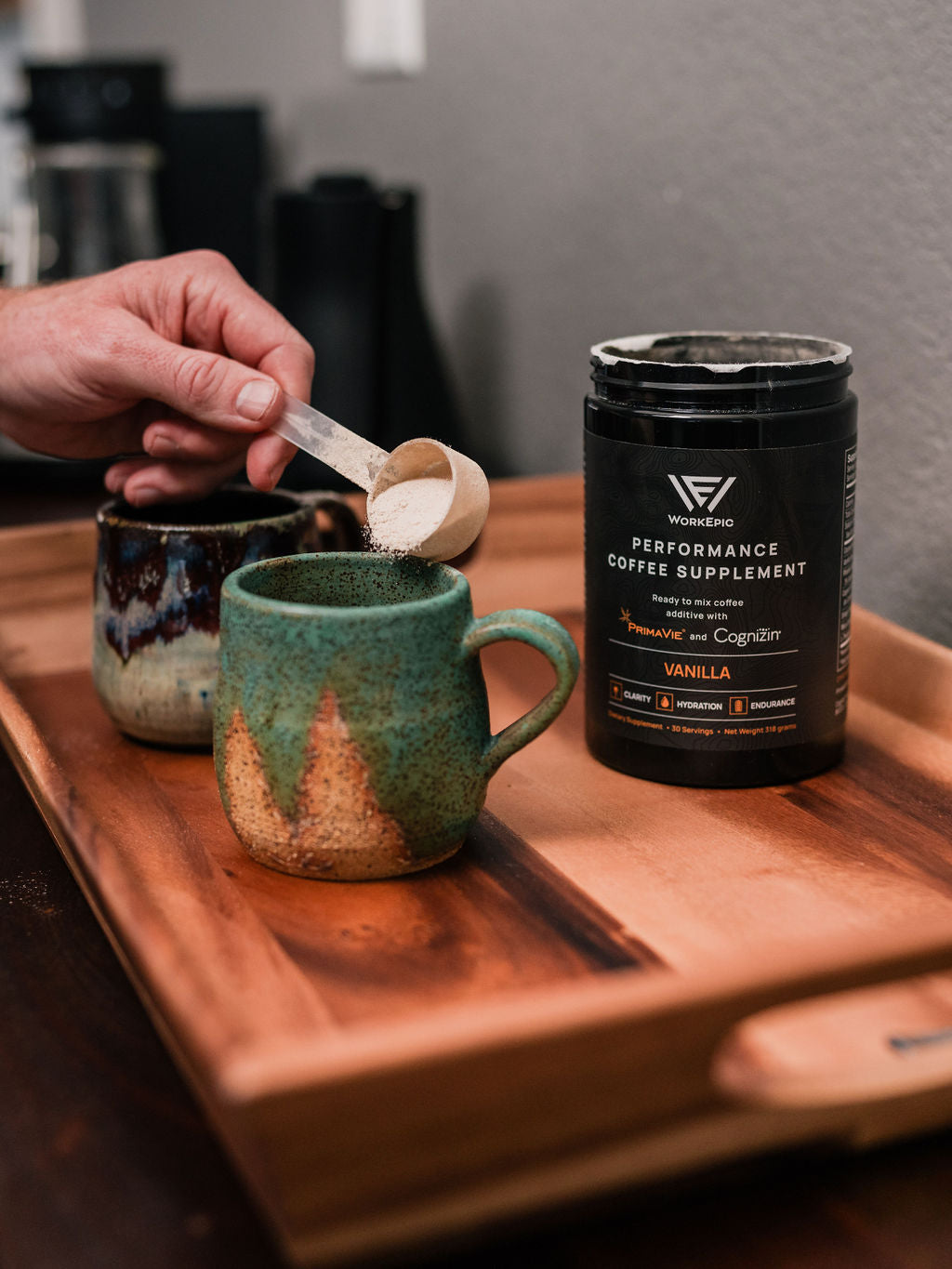 Person measuring a performance coffee supplement into a mug on a wooden tray.