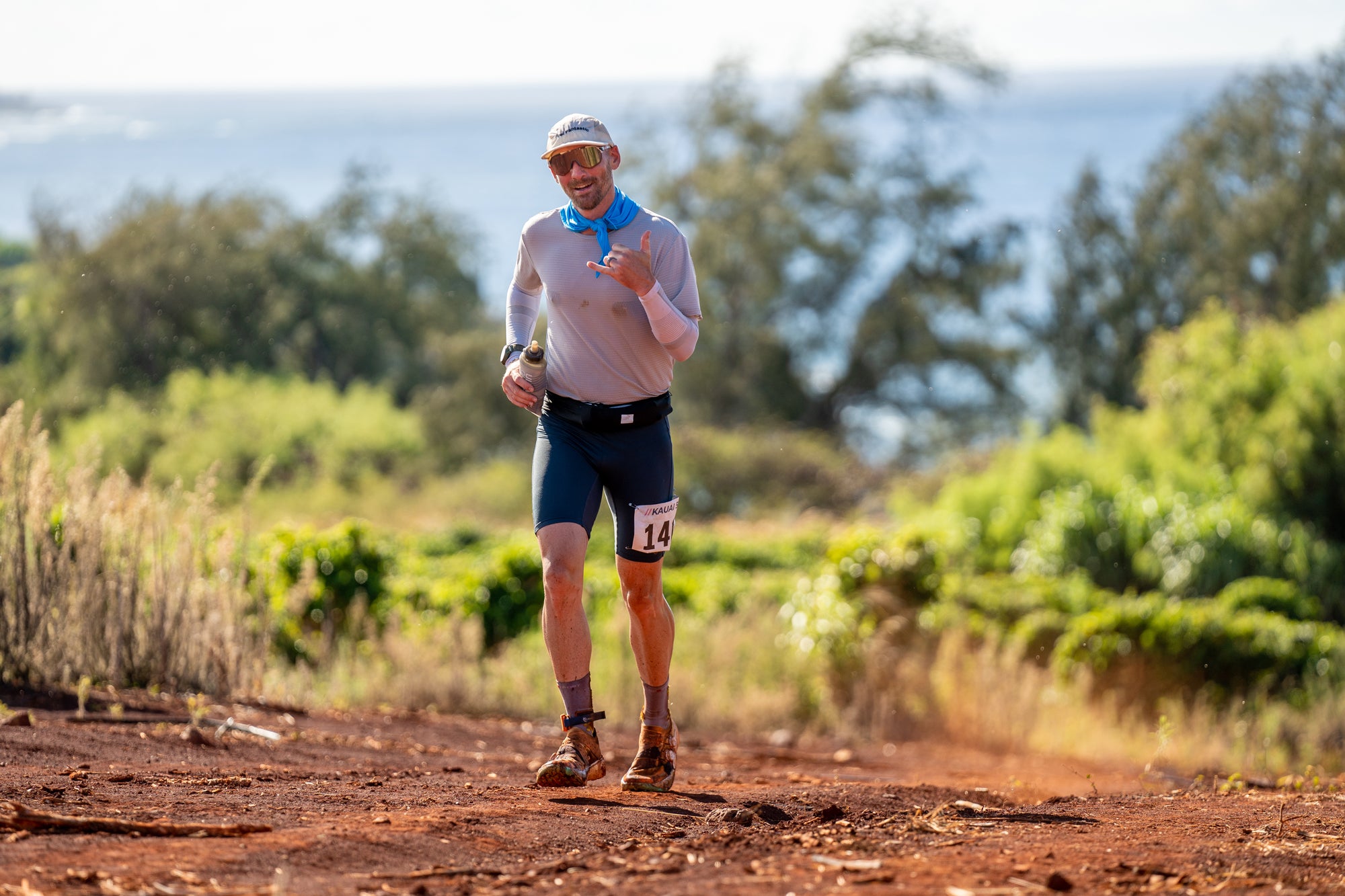 Man running on a dirt path with greenery and a blue sky in the background